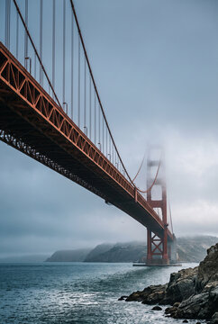 Golden Gate Bridge Tower Emerging Through Coastal Fog Above Turquoise Ocean and Rocky Cliffs
