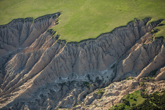 Aerial view of the rugged, eroded rock formations and deep gullies of Badlands National Park, with vibrant green prairie grass atop the cliffs in Interior, South Dakota, United States.