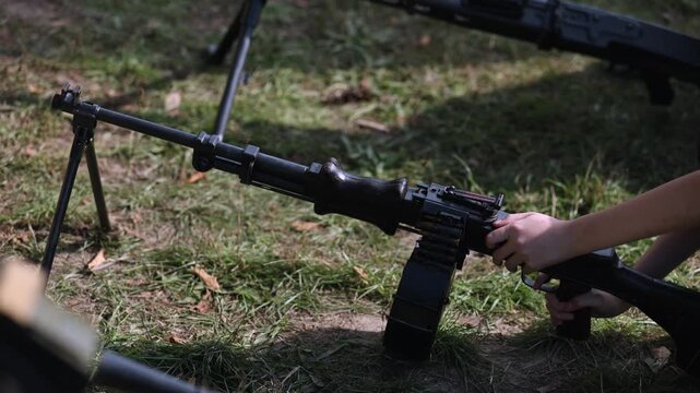 Unidentifiable person reloading an old soviet degtyaryov light machine gun with a large pan magazine during a military training exercise, showcasing the firearm's historical mechanism