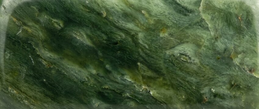 Green nephrite jade stone texture. Macro shot of polished natural mineral surface. Abstract dark green marble pattern