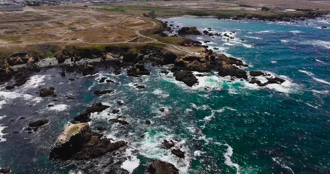 Aerial view of the rugged coastline with rocky cliffs, crashing waves, and a coastal path in Fort Bragg, California, United States.