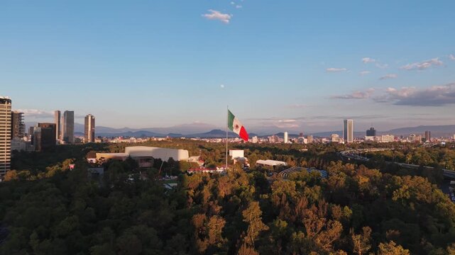 Aerial view of the Bosque de Chapultepec park with the large Mexican flag waving, surrounded by the urban skyline of Mexico City at sunset in Mexico City, Mexico City, Mexico.