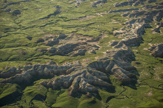 Aerial view of Badlands National Park featuring rugged rock formations, deep gullies, and vibrant green grassy plains in Interior, South Dakota, United States.