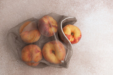 Fresh flat peaches inside a reusable mesh produce bag placed on a neutral light colored background © ir1ska