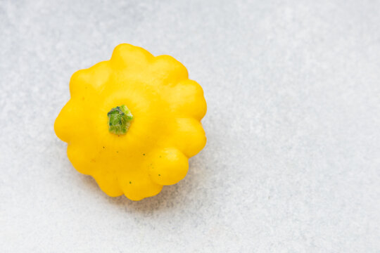 Single yellow scallop squash sits centered on a light gray textured background