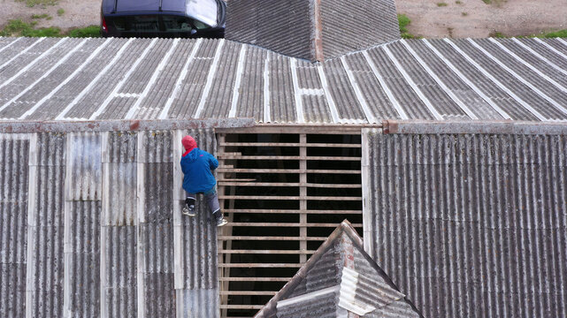 Aerial view of a worker in a blue jacket repairing a corrugated roof with exposed wooden rafters in Latvija.