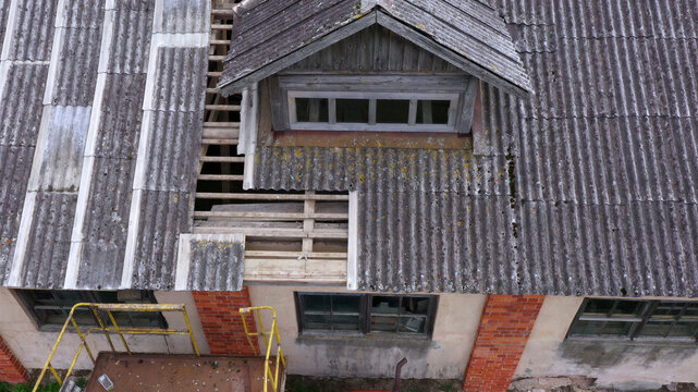 Aerial view of a building roof undergoing repairs with exposed wooden rafters, corrugated panels, a dormer window, and yellow scaffolding visible below in Latvija.