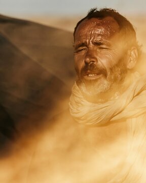Moroccan man with a weathered face and sweat on his brow, squinting under a blazing sun in a dry landscape for travel and culture