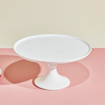 Empty white ceramic cake stand with a glossy finish on a blush rose background, a clean blank mockup for holiday and confectionery templates