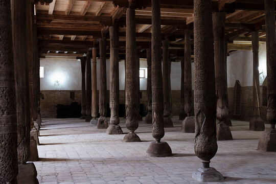 Carved wooden columns inside Juma Mosque in Khiva, Uzbekistan. Ancient hypostyle prayer hall with intricate woodwork and brick floor, ideal for travel and heritage publications.