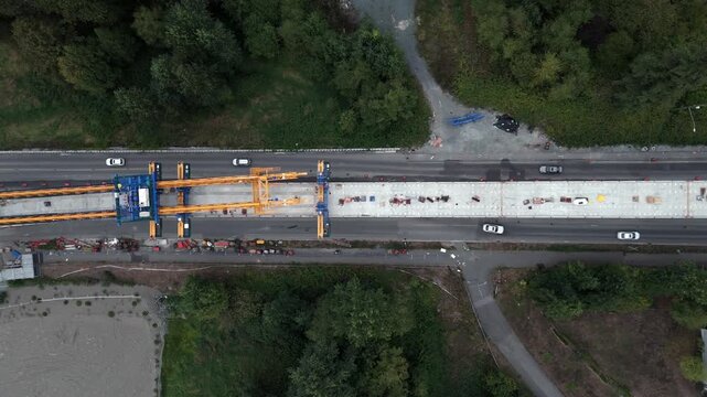 Top-down View Of Yellow Launching Gantry Crane Operating On An Elevated Skytrain Concrete Guideway Along A Highway In Surrey, BC, Canada. - aerial shot