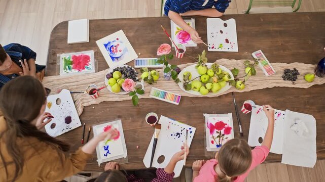 Caucasian children painting still life with watercolor during master class with female teacher, high angle shot. Footage ideal for art school promotions and creative childhood education campaigns