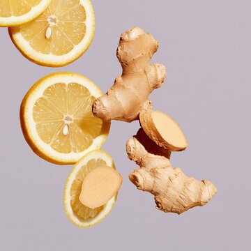 Fresh lemon slices and ginger root falling through the air, juicy and fibrous textures on a gray background for tea and cafe menus