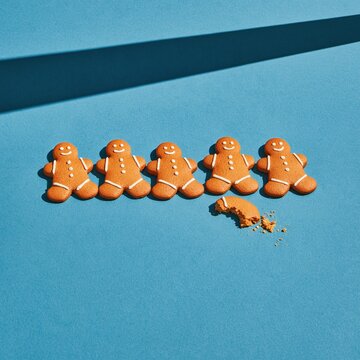 Gingerbread man cookies in a row with one broken figure on a cobalt blue background, matte baked texture for food magazines and packaging