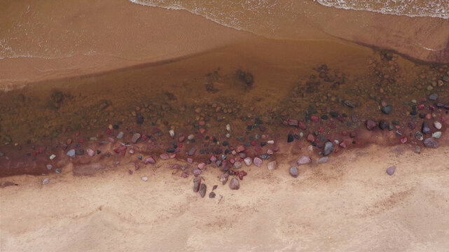Aerial view of a sandy beach with colorful stones along the shoreline and gentle waves in Latvia.