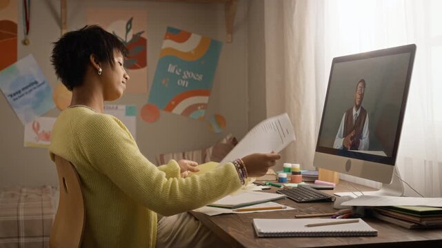 African American teenage girl checking paper assignments during online tutoring video call on computer screen. Clip suitable for distance learning ads or e learning educational campaigns