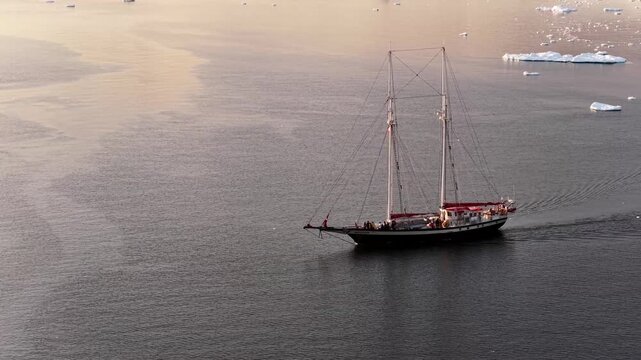 Aerial view of a classic two-masted sailboat sailing through the calm waters of the Ilulissat Icefjord in Ilulissat, Avannaata Municipalit, Greenland.