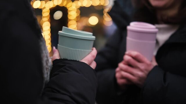 Girls Drinking Mulled Wine At Christmas On A Street Against Blurred Garland Lights