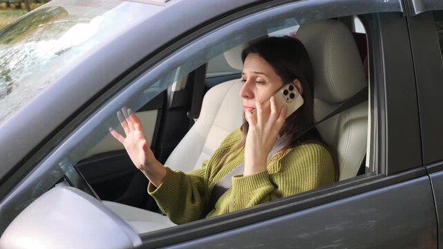 Woman shouts during emotional phone argument from driver seat, gesturing with her free hand. Frustrated driver conveys annoyance and personal conflict through emphatic speech and animated movement.