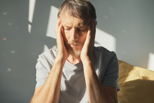 Man experiencing Headache, holding his head, illuminated by sunlight