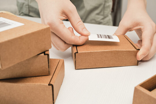 Hands applying shipping label with barcode to cardboard package