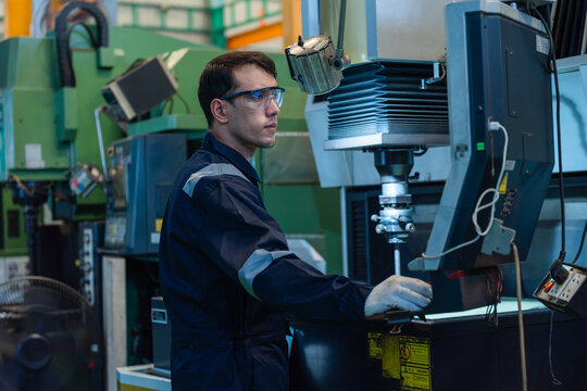 Male technician operating CNC EDM machine in industrial factory setting professional engineer controlling metal processing equipment in manufacturing plant