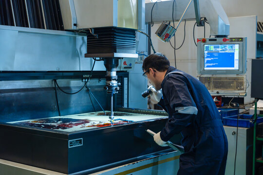 Male technician using flashlight to inspect EDM machine process professional engineer controlling precise metalworking equipment in industrial manufacturing factory