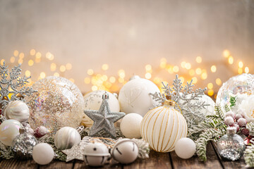 Fototapeta premium A Christmas background featuring elegant white and silver baubles, glittering stars, jingle bells, and snowflakes on rustic wood, set against a warm backdrop with twinkling lights and copy space.