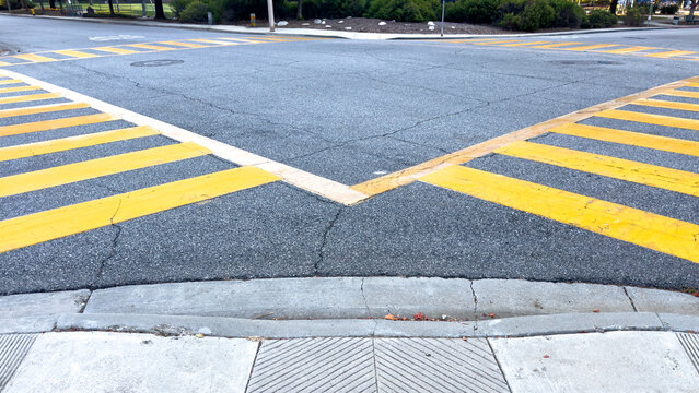 bright yellow painted zebra crosswalk stripes meet at a street intersection asphalt road with concrete sidewalk curb ramp