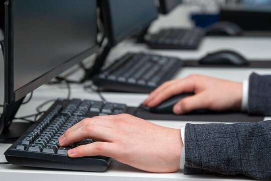 Close-up shot of hands using a computer keyboard and optical mouse on an office desk. Office workspace setting with multiple monitors, concept of software development, office work, data entry