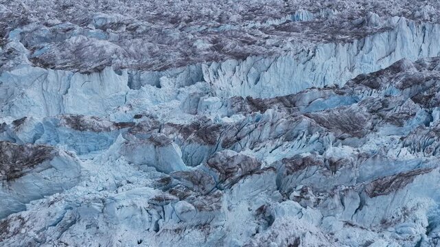 Aerial view of the massive Ilulissat Icefjord featuring deep blue crevasses and rugged ice formations across the arctic landscape in Ilulissat, Avannaata Municipalit, Greenland.
