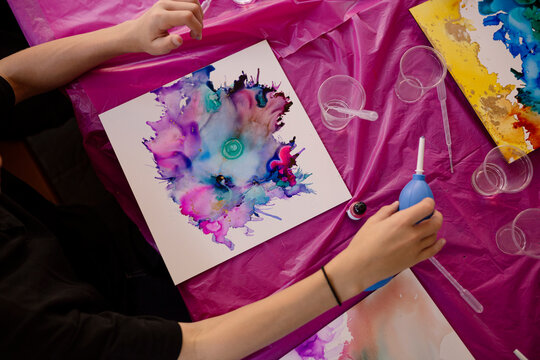 Artist using air blower to create colorful abstract alcohol ink painting.