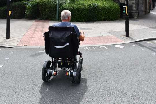 Male on a disability scooter crosses a road on his scooter at a pelican crossing. The disability vehicle allows him to get out and about on his own giving him independence and freedom to move about.