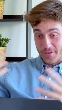 Handsome male employee having a remote work conversation and gesticulating during an important video call with colleagues, smiling and explaining project details from his modern office