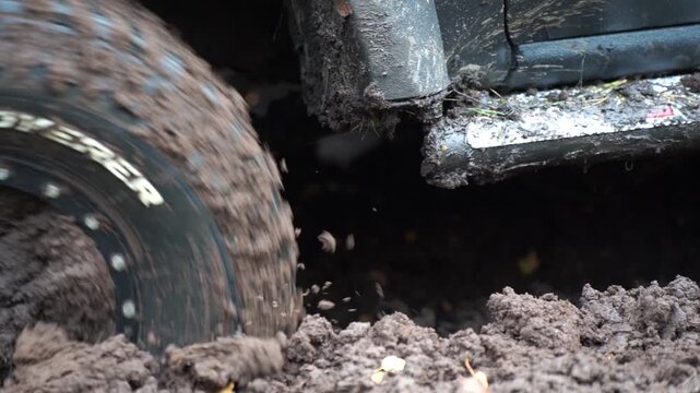 Rotating off-road tire throws small clods of mud beside the vehicle side step as it moves through a rut, illustrating soft-ground traction in recreational trail driving