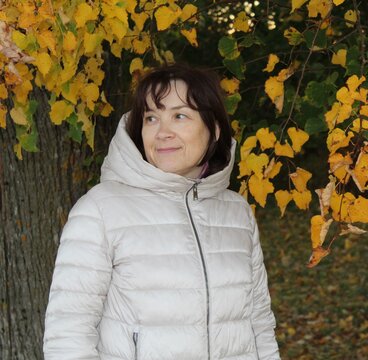 Mature Woman in White Puffer Jacket Smiling in Autumn Park.

