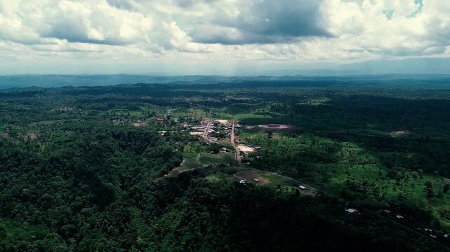 Drone footage presents a wide aerial view of dense tropical rainforest across Ecuador's Oriente. The green canopy covers rolling terrain and distant ridgelines, reaching a hazy horizon beneath a brigh
