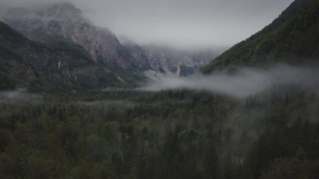 An Aerial of clouds and mist hanging above the woods and mountains in the Logarska Dolina Valley, Slovenia