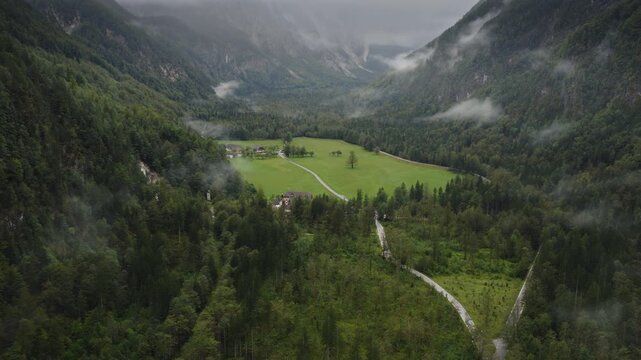 An aerial of the Logarska Dolina valley and small village with distant mountains and clouds, Slovenia