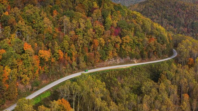 Cars driving on Blue Ridge Parkway in autumn season. Scenic route between majestic mountain hills covered in golden and scarlet leaves.