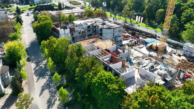 Highangle drone shot showing the progress of a new apartment complex construction surrounded by green trees in an urban area. Ideal for real estate development and urban planning content.