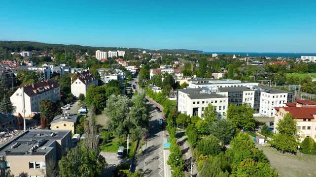 A highangle aerial shot showcasing the urban landscape of Sopot, Poland, featuring lush green trees, residential architecture, and the distant blue horizon of the Baltic Sea.