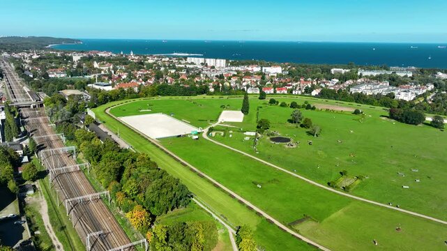 A highangle aerial shot showing the lush green fields of the Sopot horse racing track, adjacent railway lines, and the blue Baltic Sea horizon. Perfect for travel and urban planning content.