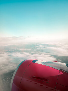 High altitude view from airplane window showing pink jet engine turbine flying above white clouds under clear blue sky. Commercial aviation travel and flight background concept.