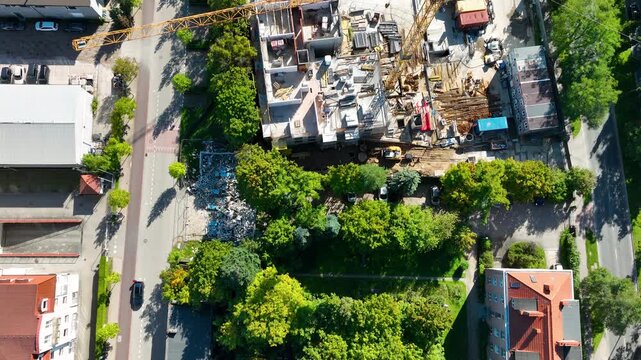 Birds eye view of an active construction site in a green urban neighborhood, featuring a large yellow crane and sustainable housing development.
