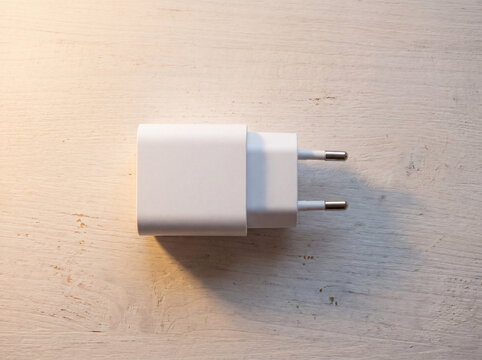 Plain white charging adapter with two round pins on a wooden desk