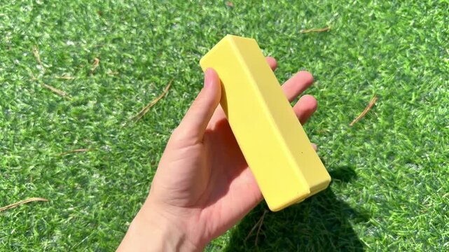 4K video of a hand holding a yellow butter shaped squishy stress relief toy outdoors. Trendy sensory fidget toy for squeezing, relaxation, tactile play and satisfying entertainment.