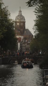 A vertical video of the Verf-en Vernisfabriek is scene in the distance near the Voorburgwal canal in Amsterdam, Netherlands