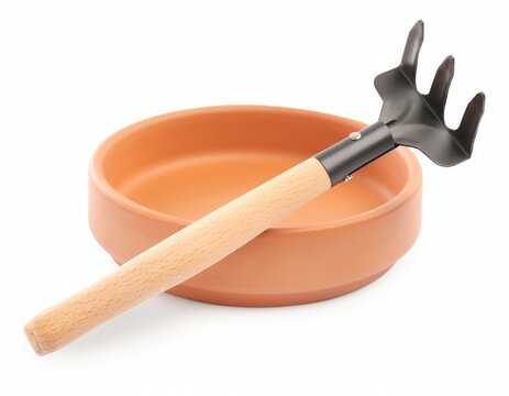 Garden rake tool resting in a terracotta saucer isolated on white background