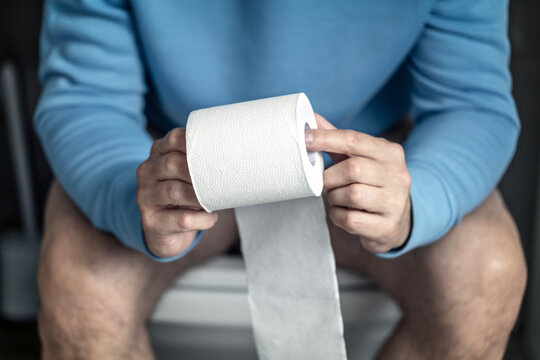 Man sitting on the toilet holding toilet roll paper tissue